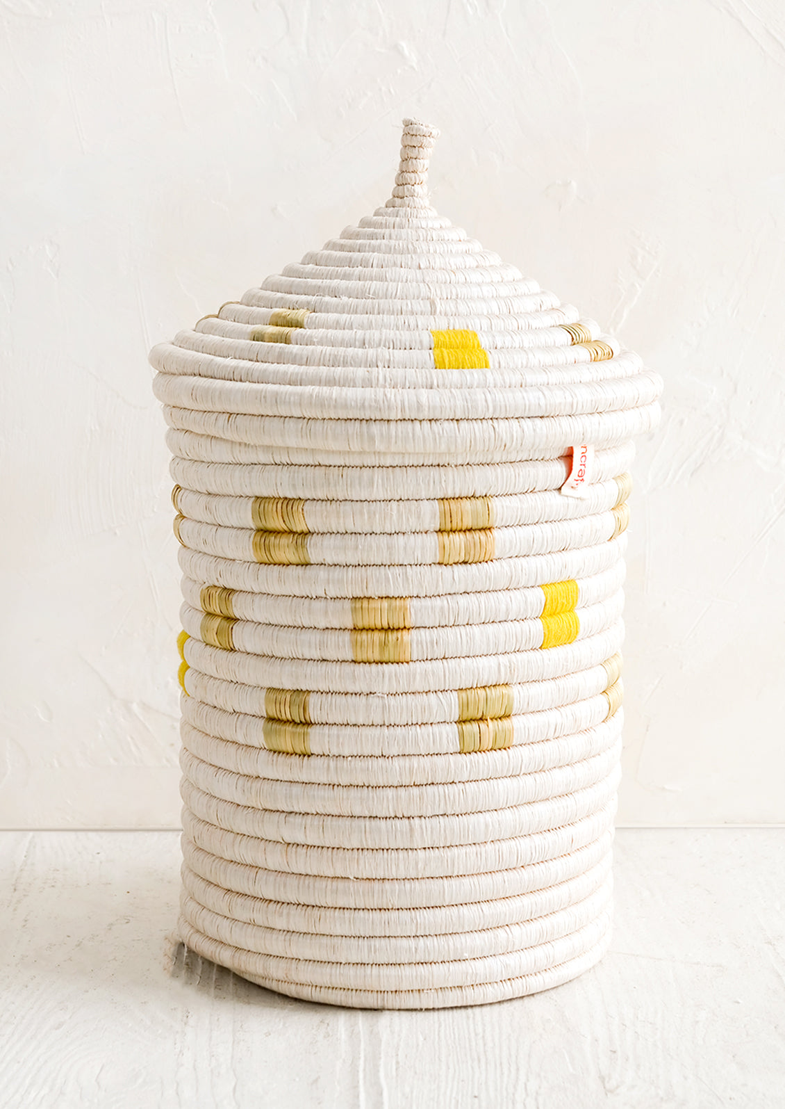 A tall woven basket with gourd-style lid in white with natural and yellow square pattern.