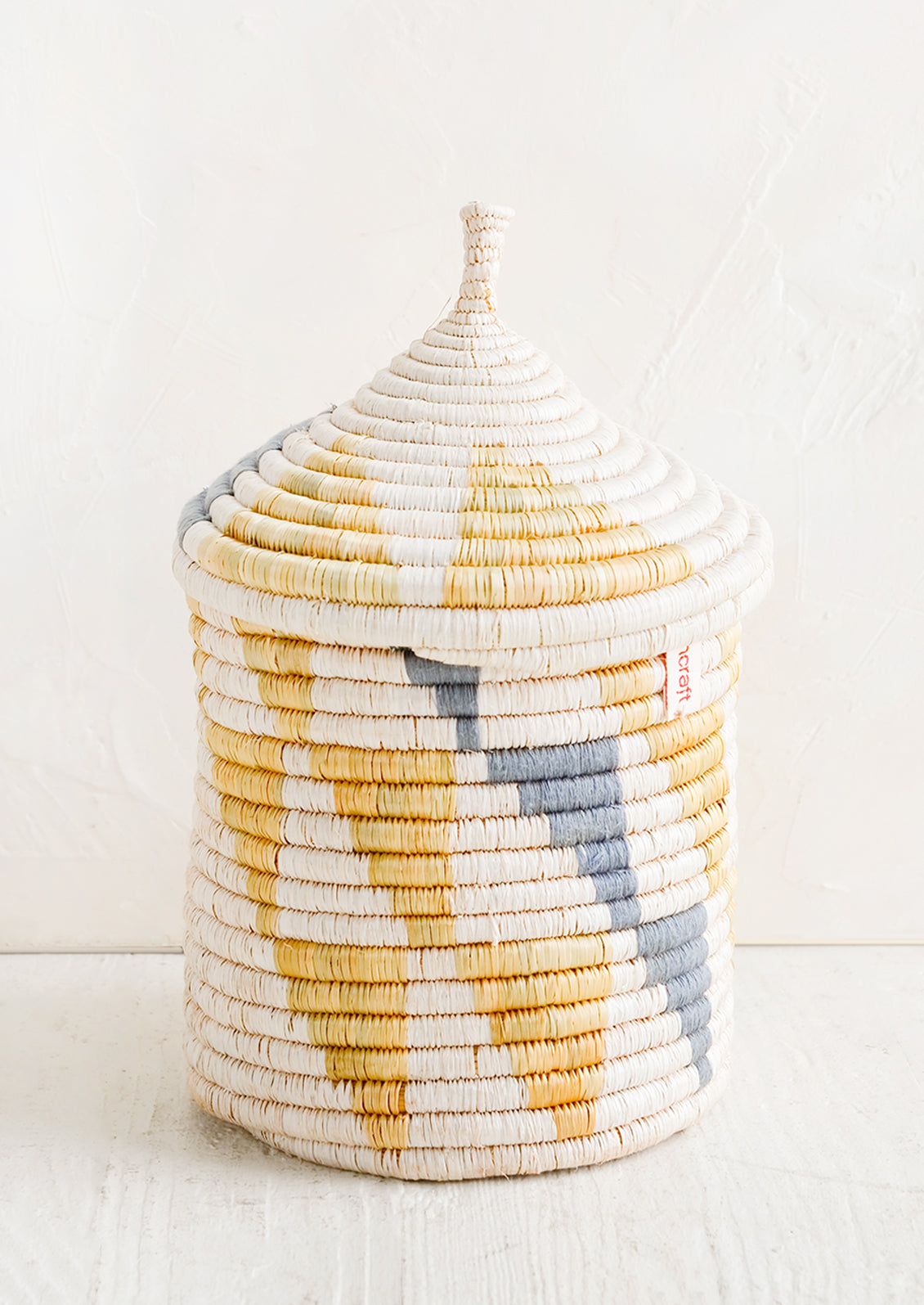 A medium woven basket with gourd-style lid in white with natural and slate grey triangle pattern.