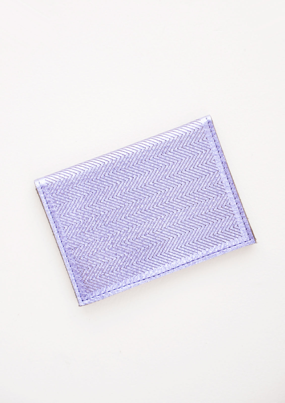 Slim metallic blue leather wallet with two interior slip pockets that folds closed with a snap, shown closed with zig zag etched pattern. 