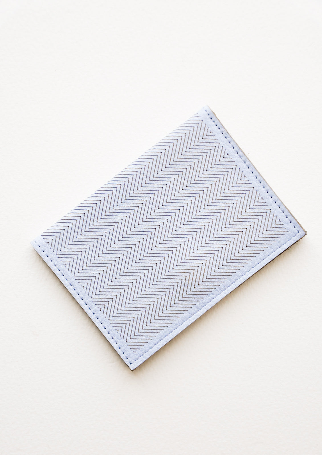 Slim light blue leather wallet with two interior slip pockets that folds closed with a snap, shown closed with zig zag etched pattern. 