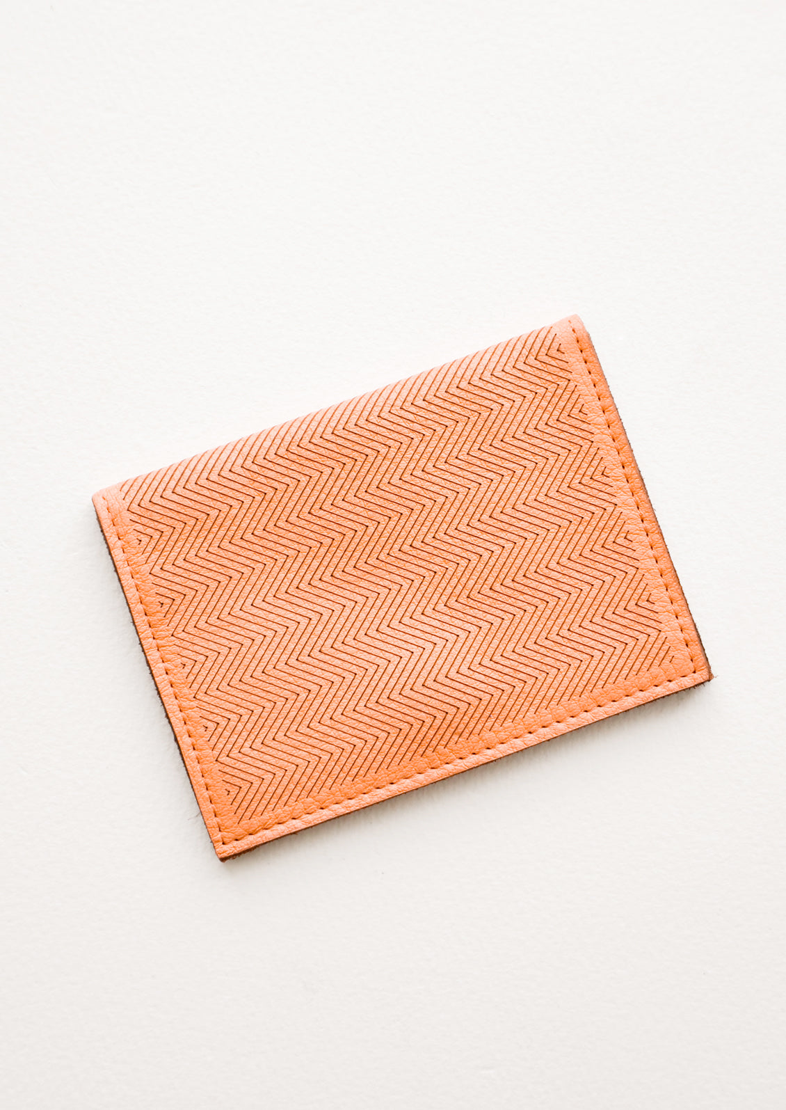 Slim terracotta orange leather wallet with two interior slip pockets that folds closed with a snap, shown closed with zig zag etched pattern. 